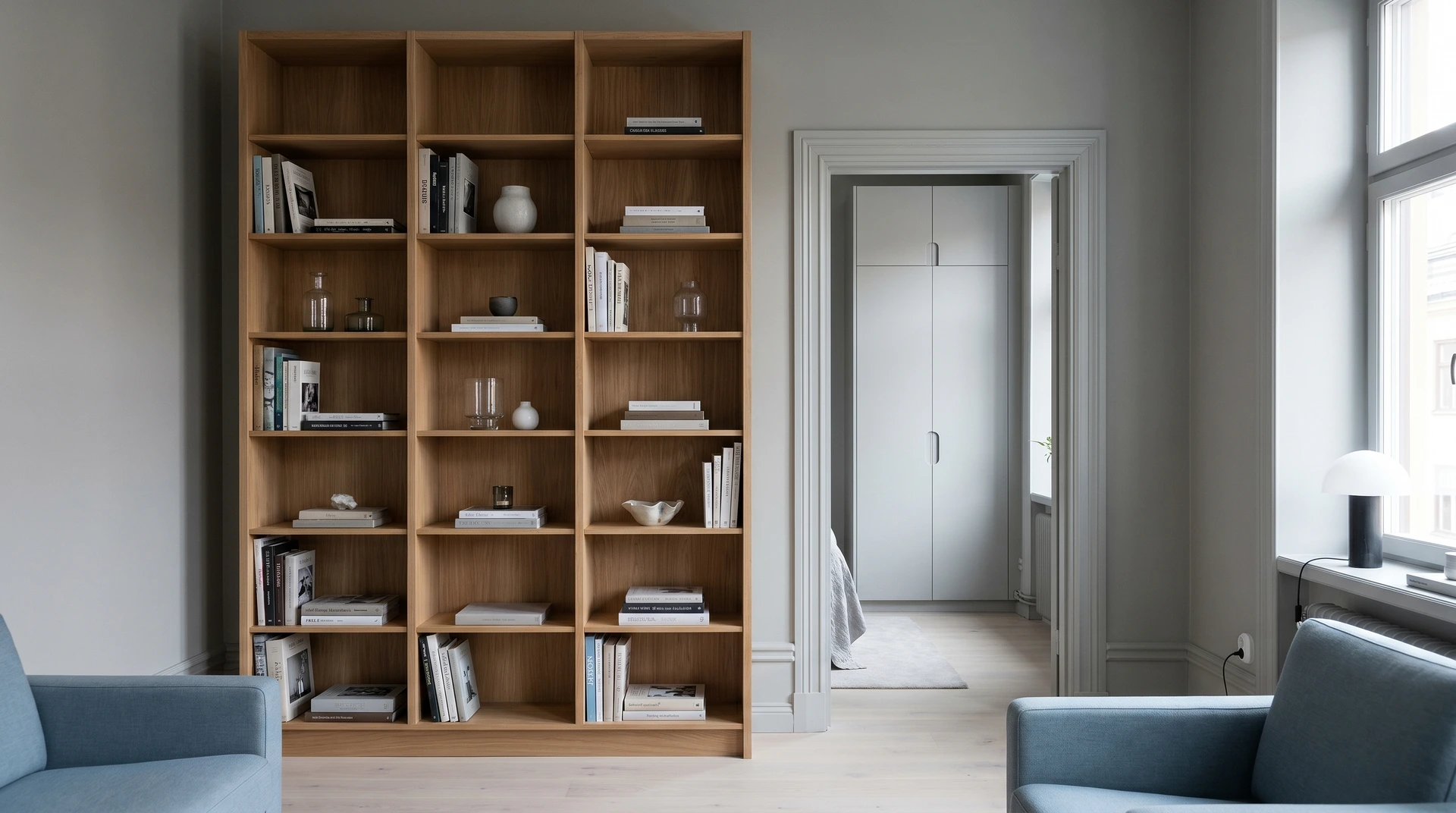 Minimalistisk bokhylla i ljust trä med böcker och dekorativa föremål.